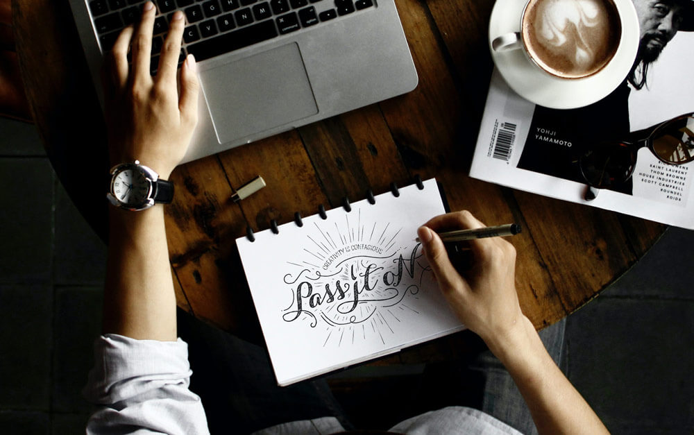 Branding Designer creating a logo design at a table with a computer and coffee
